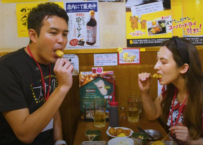 Shizuka and host Katsu eating deep-fried skewers at an izakaya.